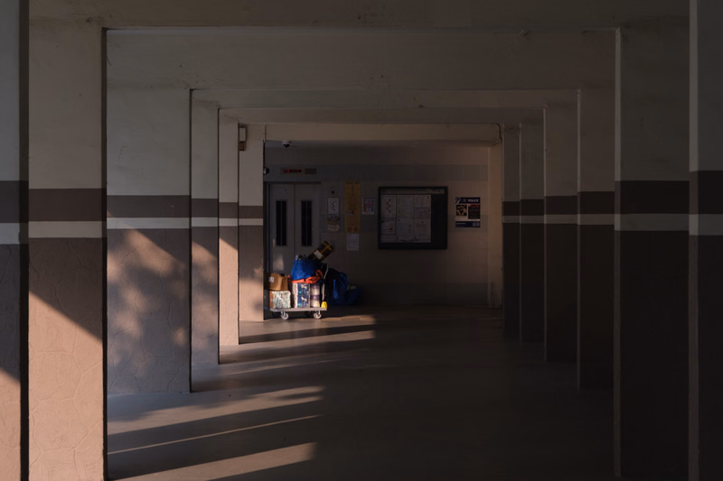 A dimly lit interior hallway with a doorway leading to another room, where some items are stored near a white notice board.