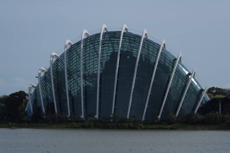 A large, modern glass dome building is situated next to a body of water under a cloudy sky.