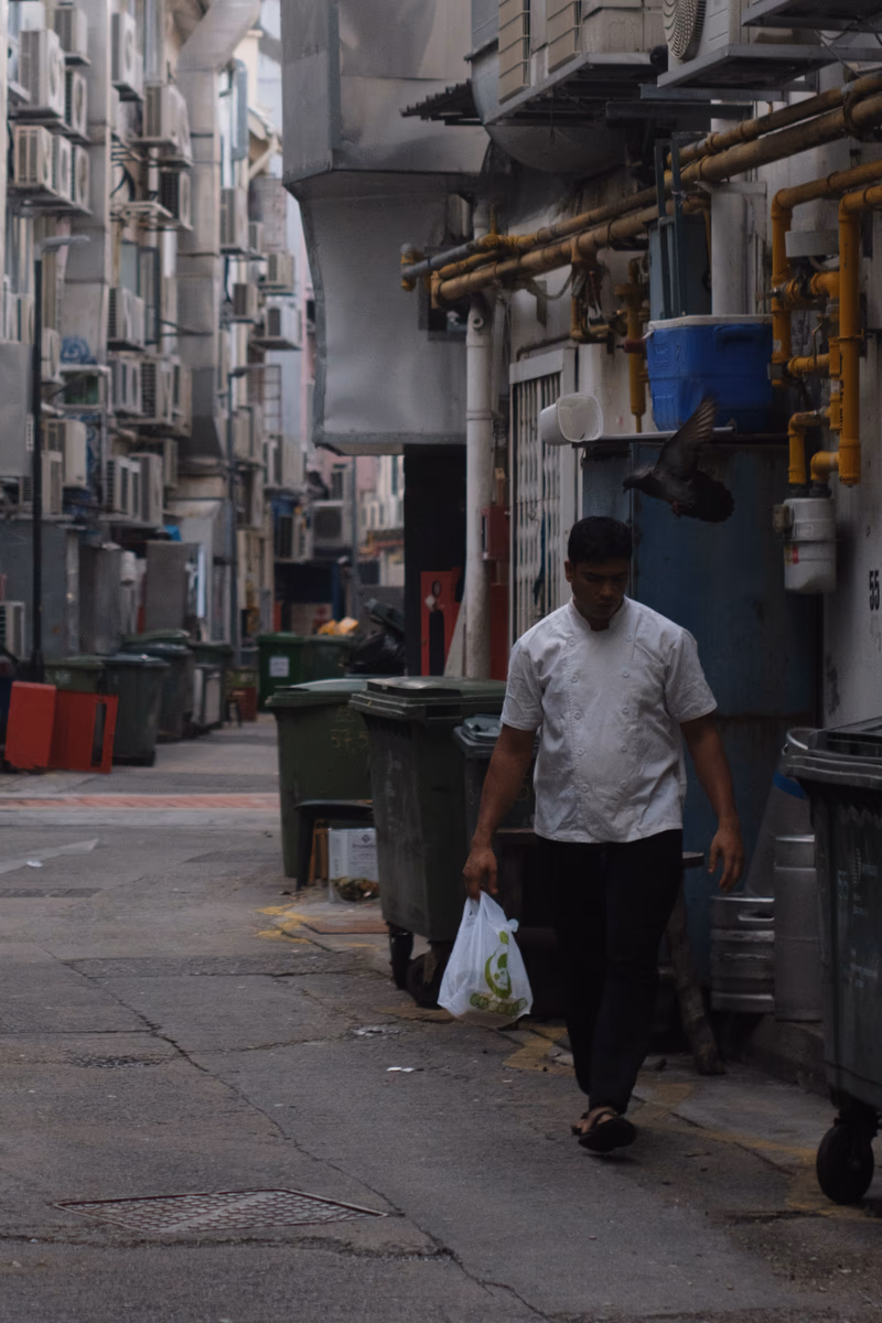 A man walking down a narrow street in a densely built area.