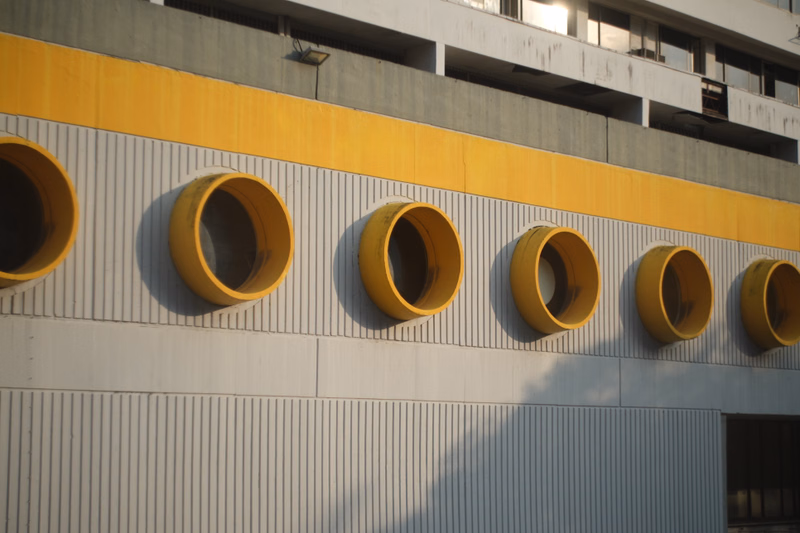 A modern building facade features a bright yellow horizontal band with a row of large, circular openings.
