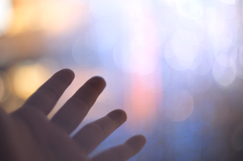A close-up of a hand reaching towards a bright, blurred background of warm and cool lights.