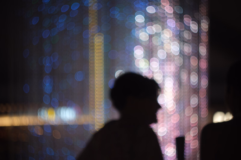 A silhouette of a person is visible against a background of colorful, out-of-focus bokeh lights at night.