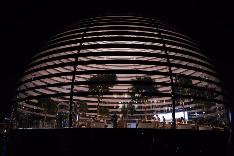 A photo of a spherical structure with horizontal slits, taken at night, showing people inside.