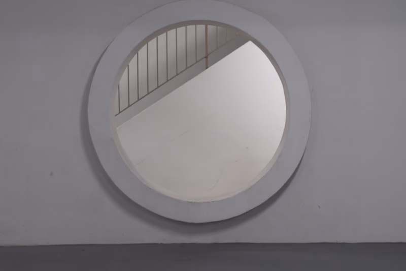 A circular mirror mounted on a wall, reflecting a staircase and part of the interior.