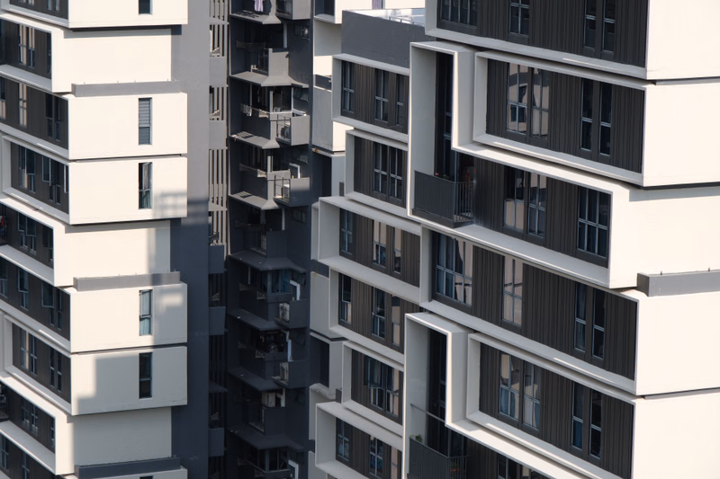 A modern apartment building with white and dark gray facades features multiple balconies and rectangular windows.