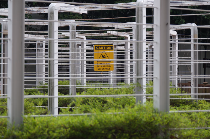 A caution sign in a garden area with plants and white poles around it.