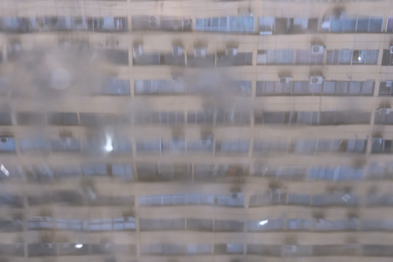 A blurred image of a tall apartment building facade with multiple rows of windows.