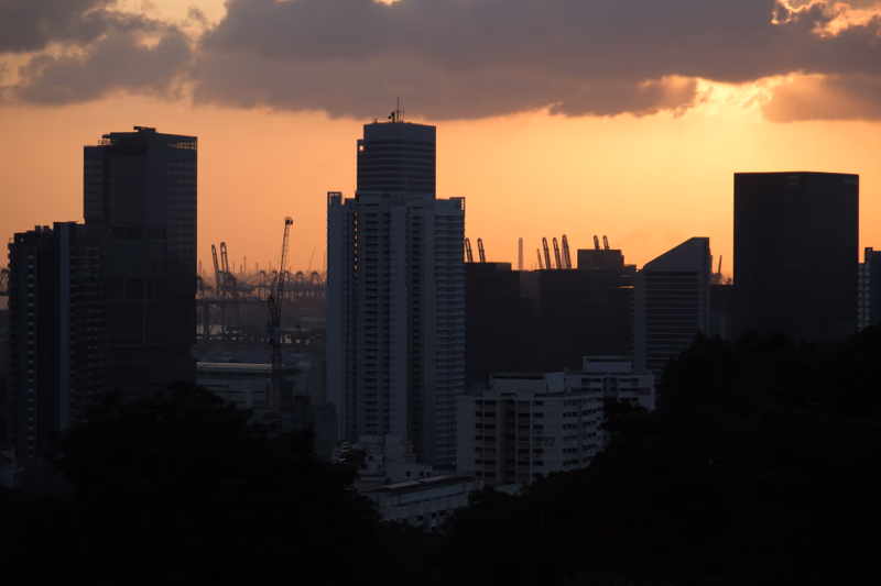 A photo of a cityscape at sunset with buildings, cranes, and a water body in the background.
