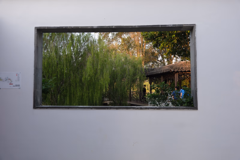 A photograph of a window reflecting a garden with lush green trees and a traditional building.