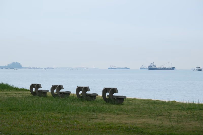 A serene coastal scene with boats in the distance and benches on the grass near the water.