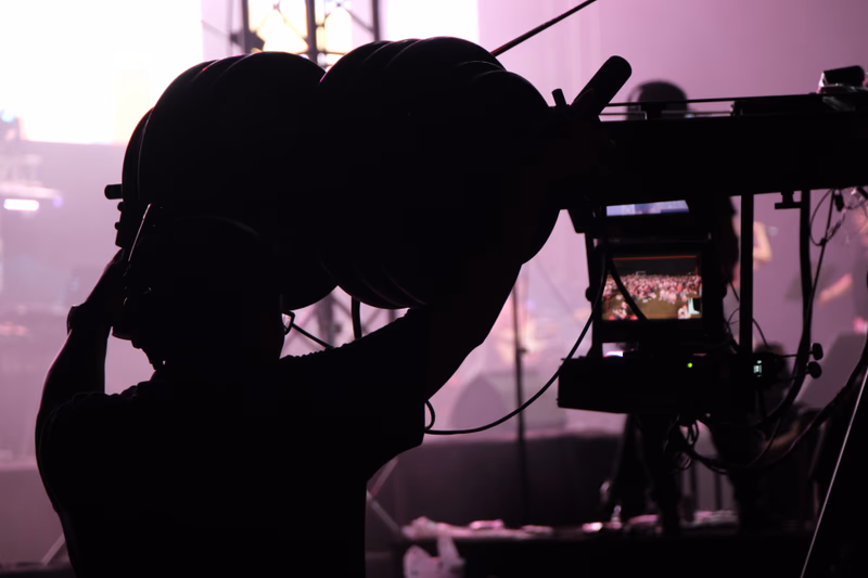 A silhouette of a person adjusting equipment, a camera, and a screen displaying a scene.