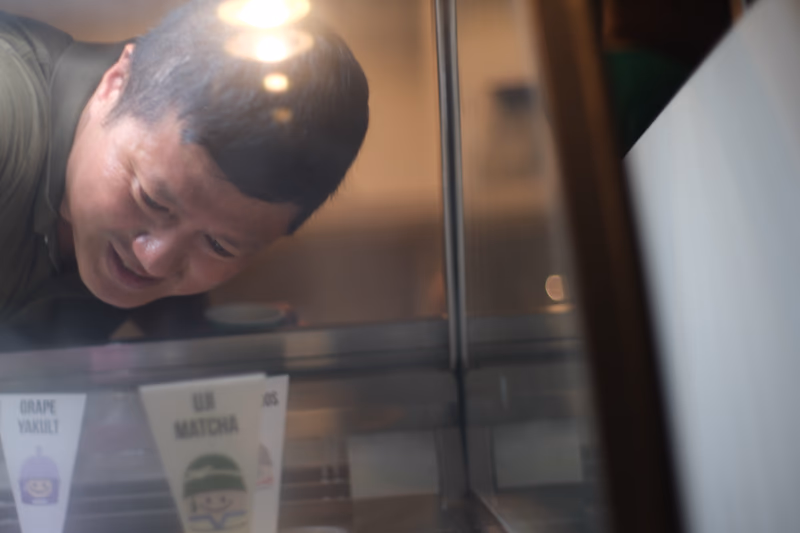 A man leaning over a display case, looking at ice cream flavors.