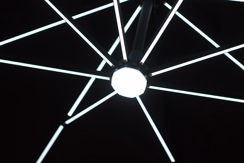 A close-up view of a modern, geometric light fixture with multiple bright white LED strips radiating from a central globe.