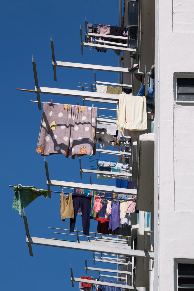 Colorful laundry hangs on multiple lines extending from the side of a white apartment building against a clear blue sky.