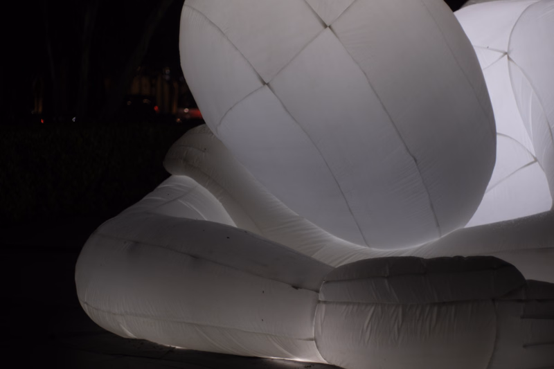 A large, smooth, white inflatable sculpture dominates the foreground against a dark background at night.