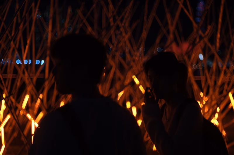A photo of two people standing in front of a complex, glowing structure at night.