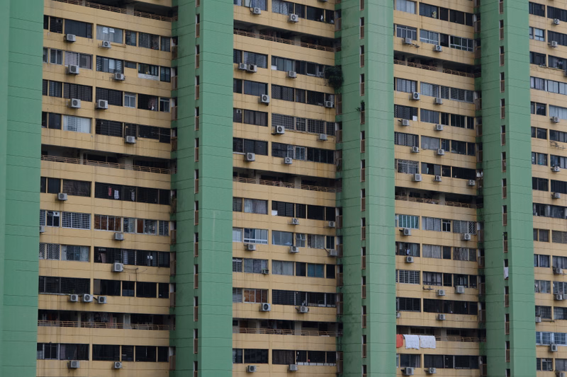 A row of tall, multi-story apartment blocks with balconies and numerous windows under a bright sky.