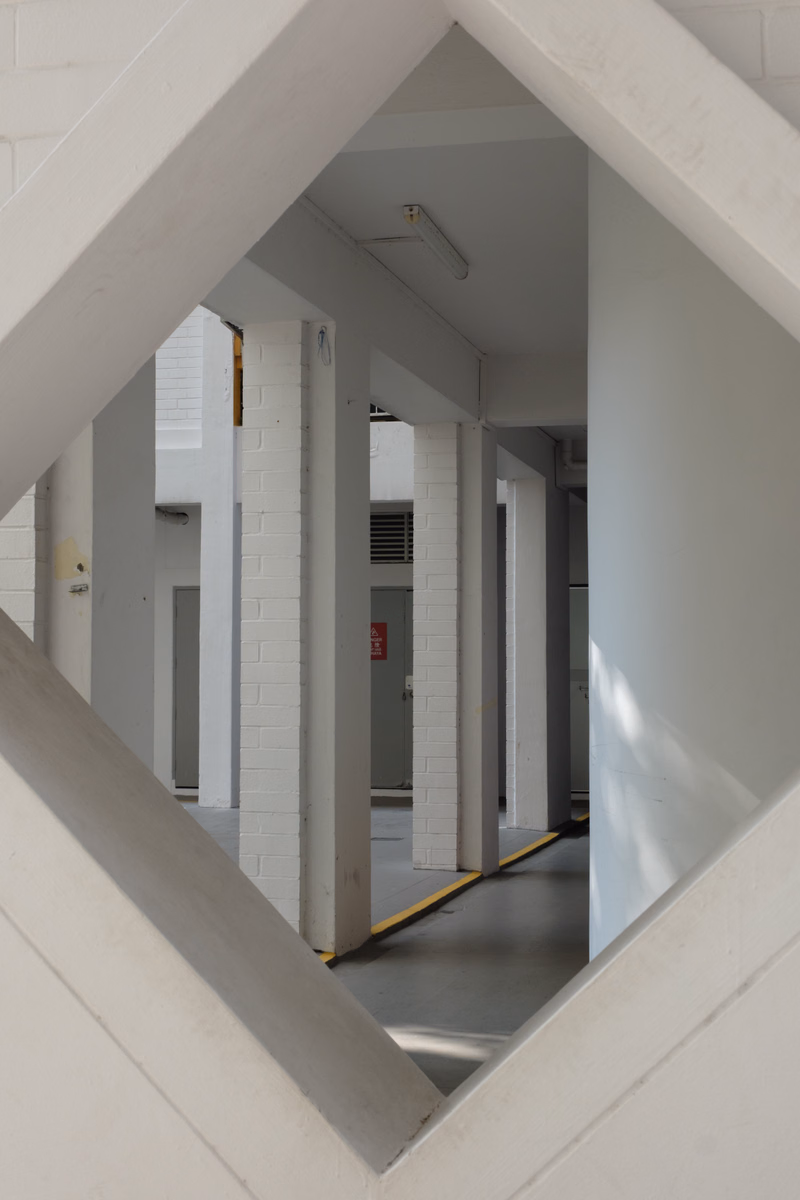 A view down a brightly lit interior hallway featuring white brick pillars and a gray floor.