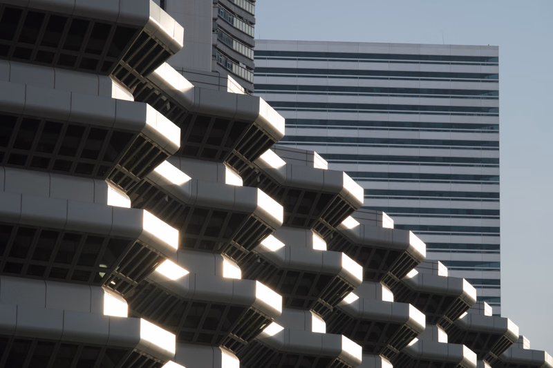 A modern office building with a distinctive, stepped facade is shown against a clear sky.