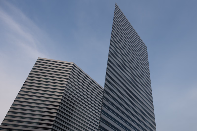 Two modern buildings with striking horizontal striped facades rise against a pale blue sky.
