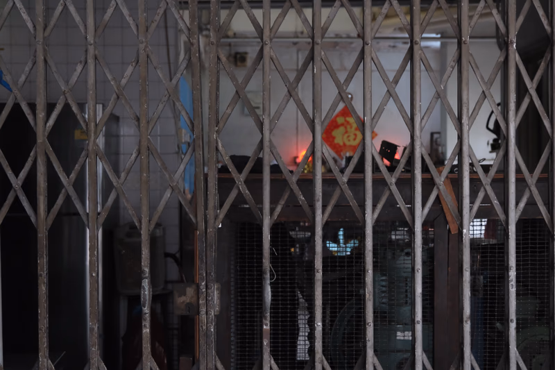 A metal gate in a dimly lit room with a red flag and Chinese characters hanging on the wall.