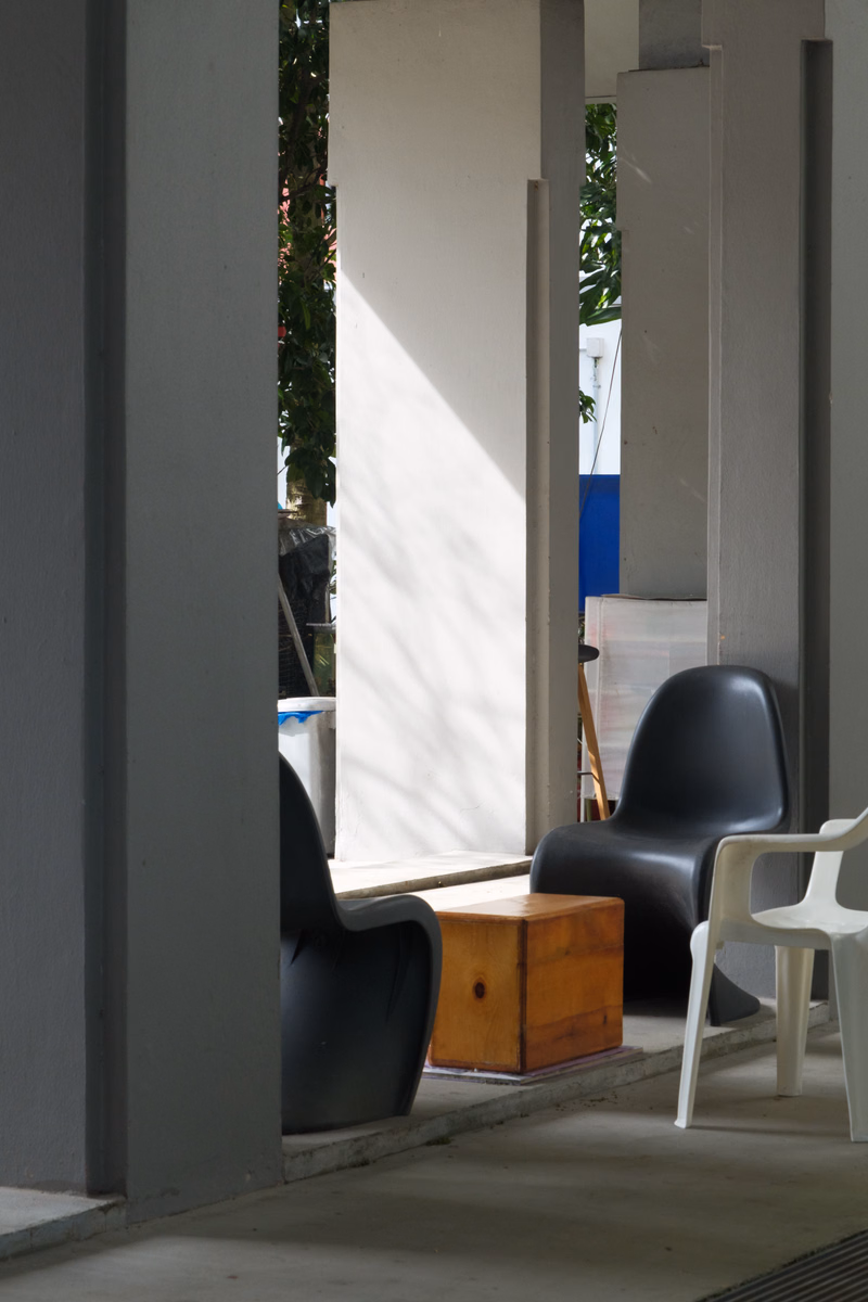 Several black modern chairs are placed on a concrete porch area with a wooden side table visible.