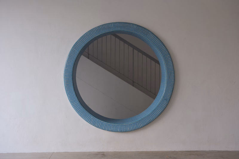 A large circular mirror with a blue tiled frame is mounted on a plain white wall.