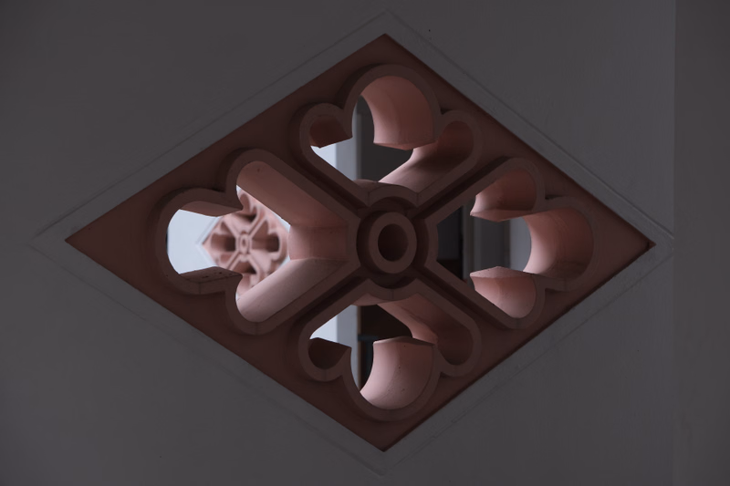 A square decorative panel featuring an intricate, symmetrical geometric pattern carved into reddish-brown stone.