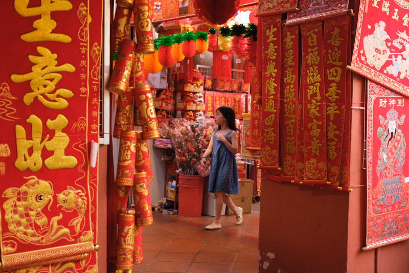 A woman walks through a hallway decorated with vibrant red Chinese New Year banners and hanging lanterns.
