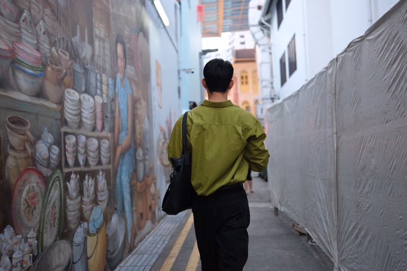 A man walking down a narrow alleyway with a mural on the side wall.