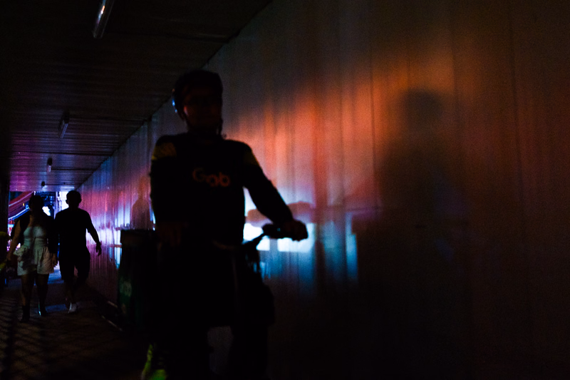 A person wearing a dark shirt with "Gob" visible walks through a tunnel illuminated by colorful lights.