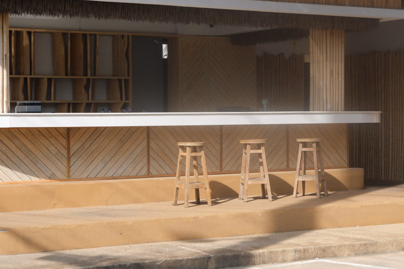 A modern outdoor bar counter with wooden stools set against a backdrop of light wood paneling.