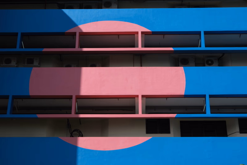 A colorful building with a large pink circle on its blue walls. The building has multiple levels with air conditioning units on the exterior.