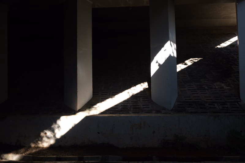Strong sunlight casts sharp shadows of pillars onto a tiled porch floor.