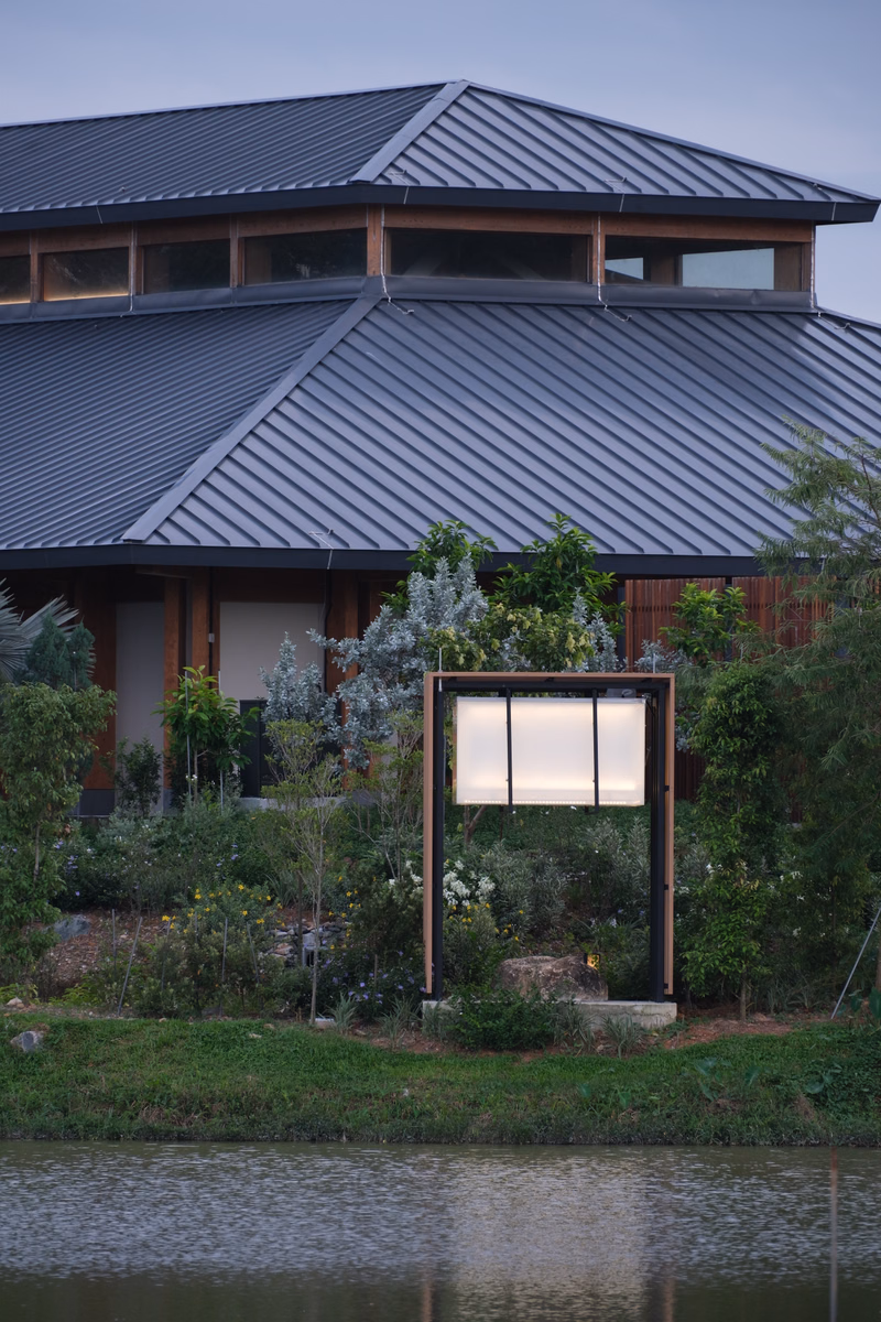 A modern house with a dark metal roof is situated near a body of water, featuring a framed window display in the foreground.