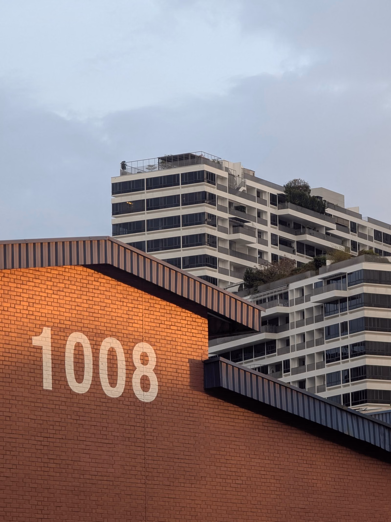 A modern apartment building with a white facade is visible behind a red brick wall displaying the number "1008".