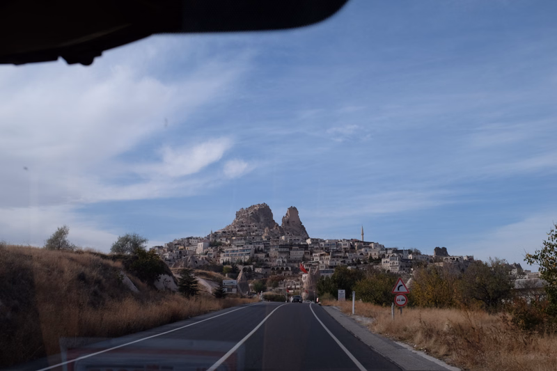A view of a historic town built on hills under a partly cloudy sky, with a road leading toward the settlement.