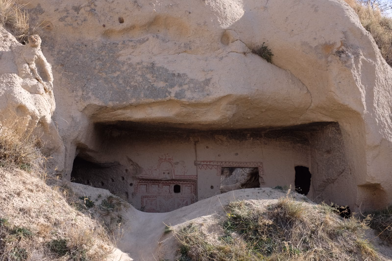 An ancient cave dwelling or tomb carved into a large, light-colored rock formation, featuring decorated niches.