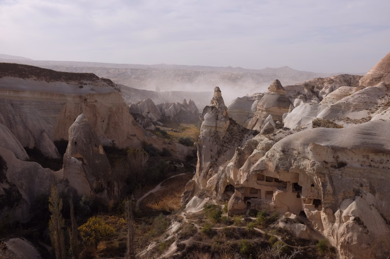 A panoramic view of Cappadocia's unique fairy chimneys and rock formations featuring cave dwellings under a bright sky.