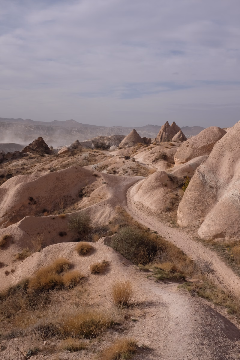 A panoramic view of arid hills featuring distinctive conical rock formations under a cloudy sky.