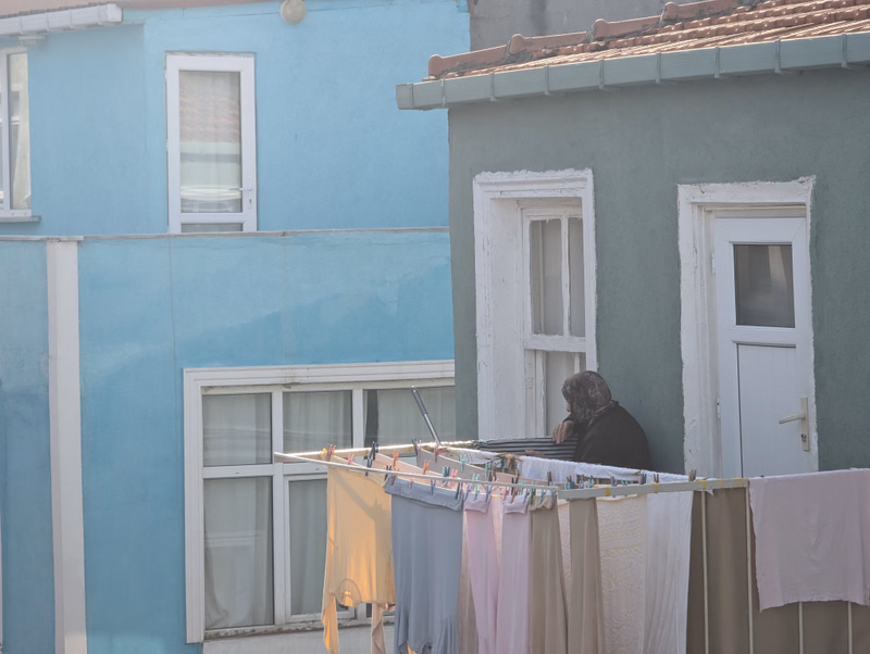 A woman hangs laundry on a clothesline outside a light blue and grey house.