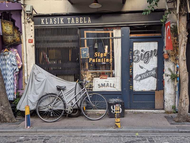 A bicycle is parked in front of a storefront with signs reading "KLASİK TABELA" and "Sign Painting".