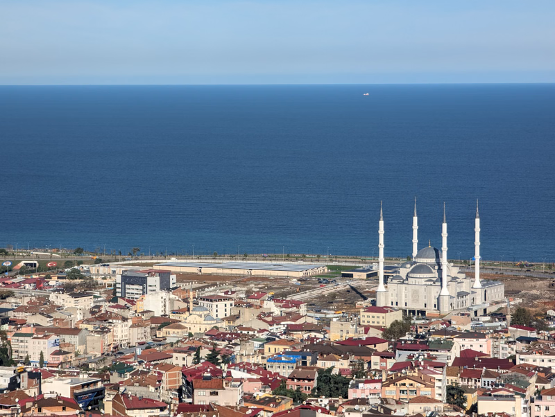 A large mosque with multiple minarets is visible near the coastline overlooking a vast blue sea, surrounded by a dense city.