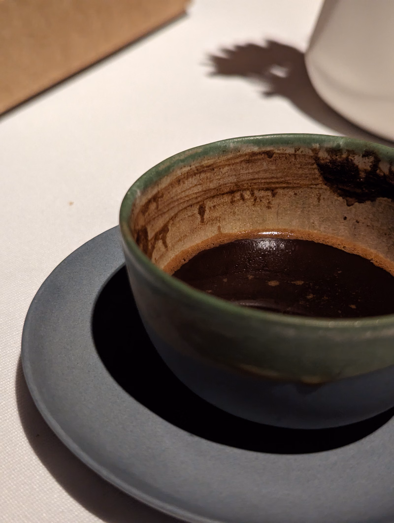A dark brown coffee is served in a small, green ceramic cup resting on a light gray saucer.