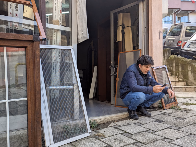 A man is working on installing a large screen door next to a doorway with glass panels.