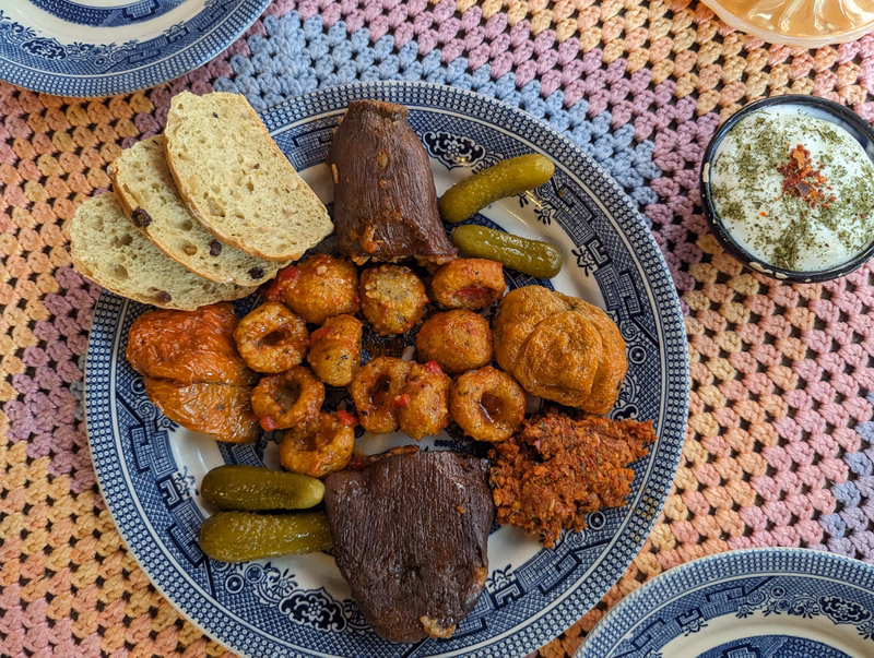 A platter of roasted meat, fried snacks, and green vegetables is served on a patterned blue and white plate.