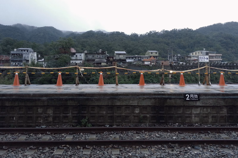 A view from a train station platform showing a town nestled among green mountains, with a sign reading "2月台 Platform".
