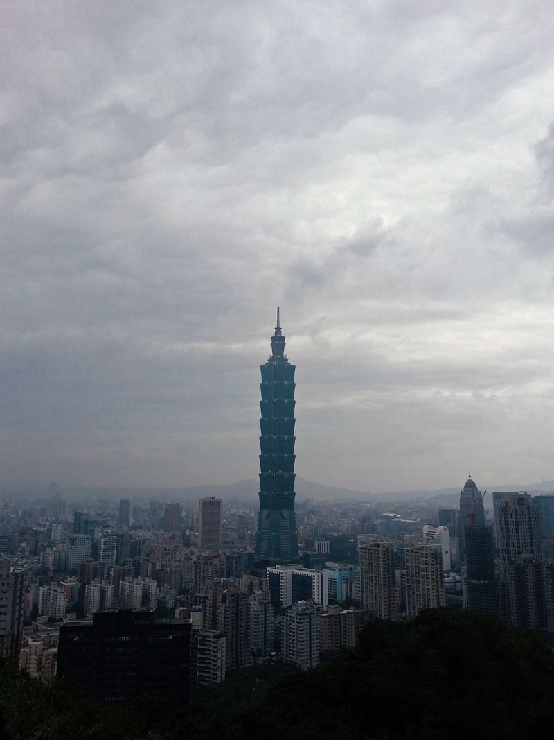 Taipei 101 skyscraper dominates the cityscape under a heavily overcast, gray sky.