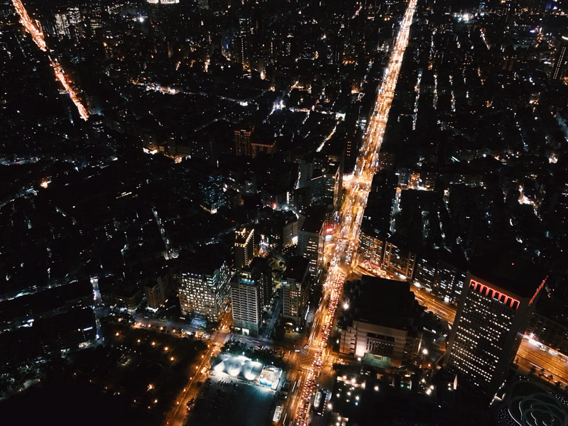 A high-angle nighttime view of a dense city street illuminated by numerous lights stretching through the urban landscape.