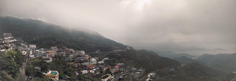 A town nestled on a steep hillside shrouded in thick, low-hanging fog and clouds.
